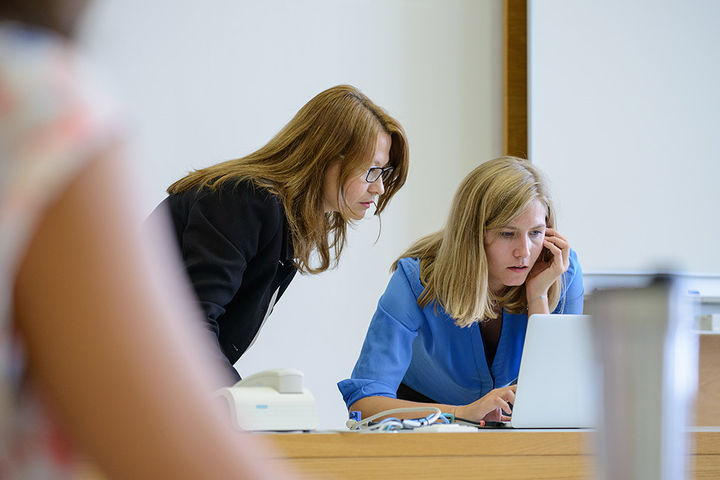 Zwei Frauen sind über einen Bildschirm eines Laptops gebeugt.